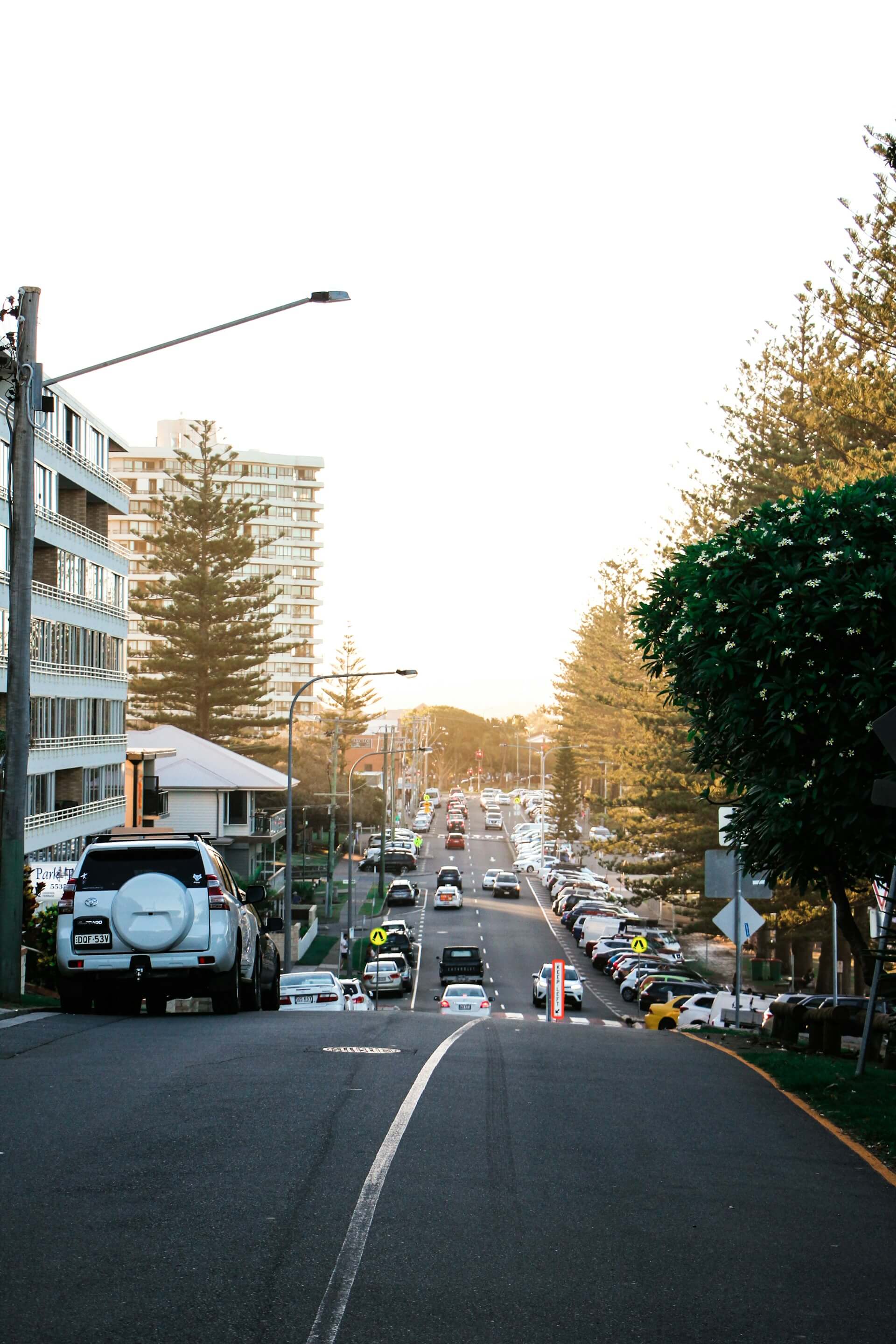 Suburban street lined with parked cars at sunset.