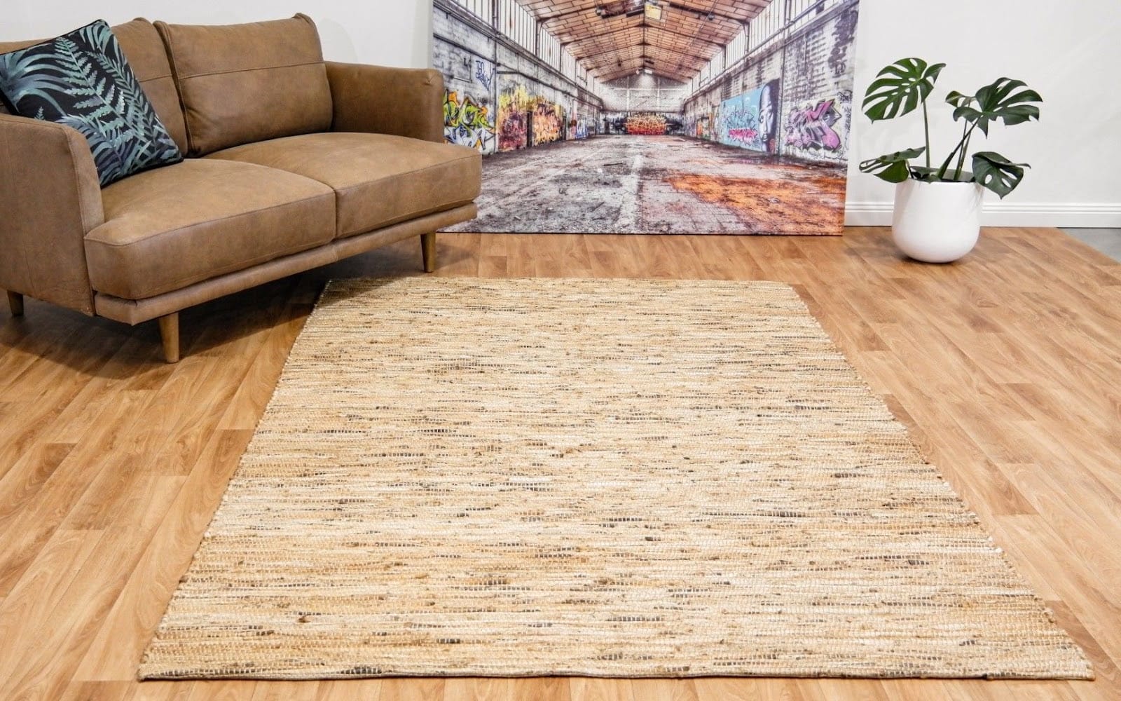 Medium-sized natural jute rug in warm beige tone placed in the centre of the room, decorated with plants and modern art.Â