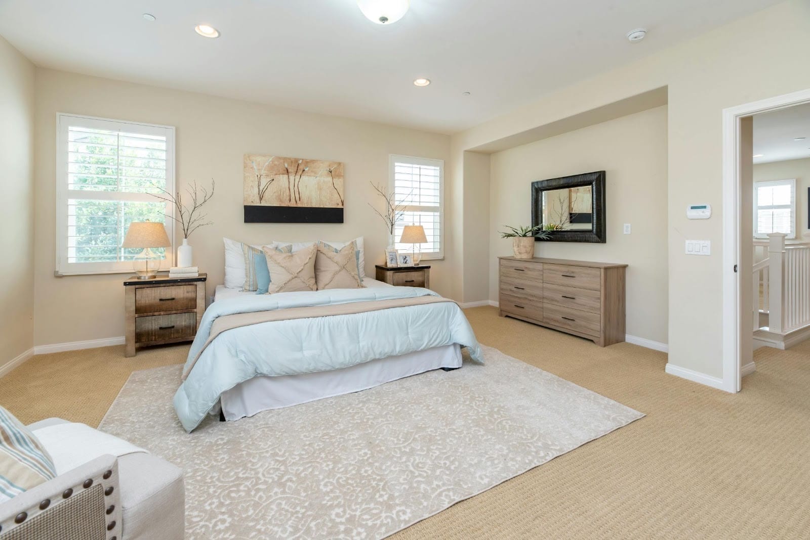 Warm, spacious and cosy bedroom with large beige rug, classic furniture and a splash of colours, such as a blue pillow.